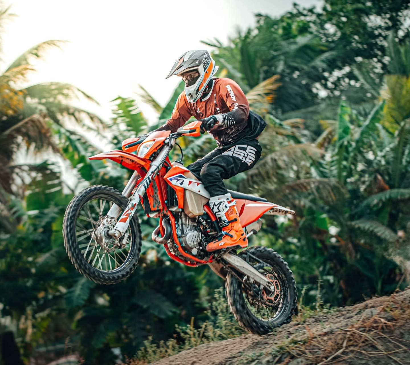 Enduro rider airborne over a jungle berm