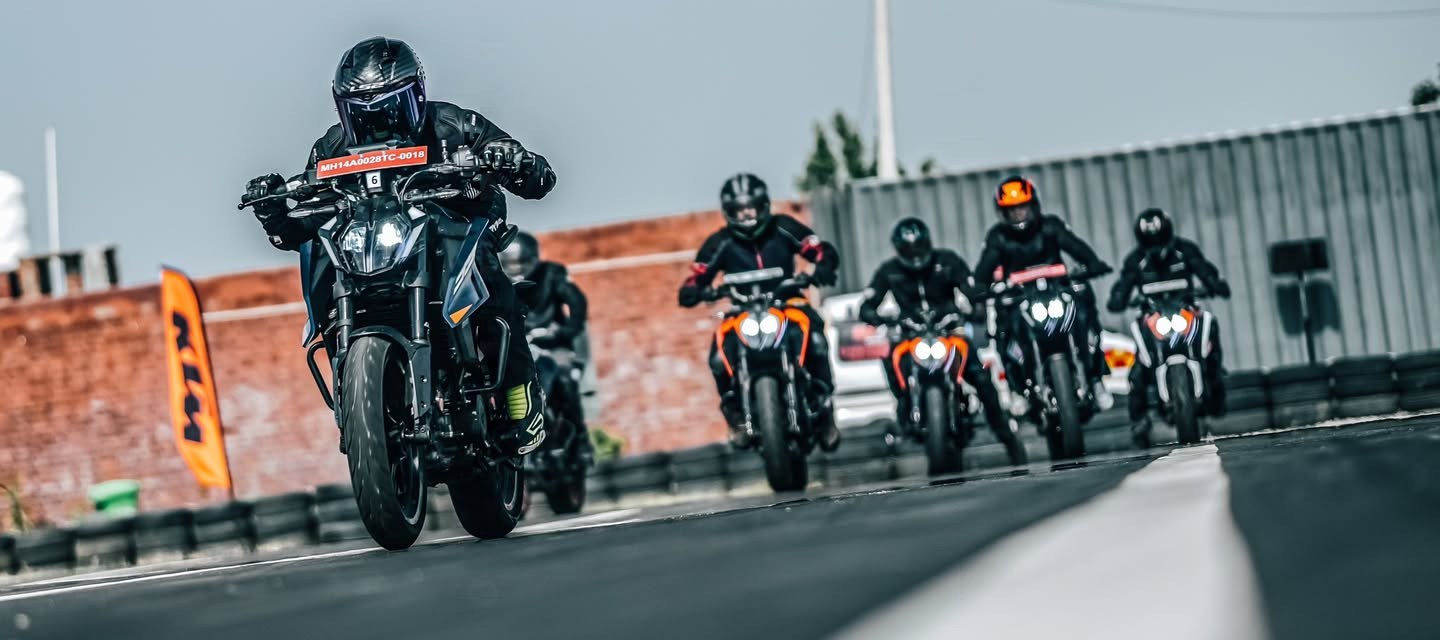 A pack of riders on orange naked bikes charging down the track toward camera